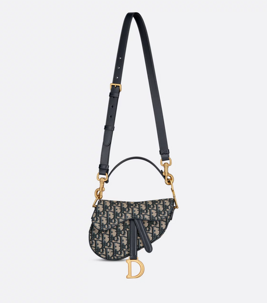 Designer handbag with black strap and gold hardware on a light gray background