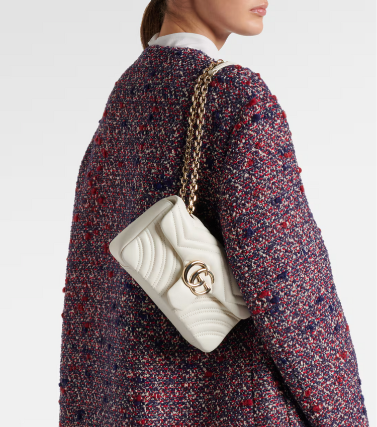 Gucci White quilted handbag with gold chain strap worn by a person in a patterned coat.