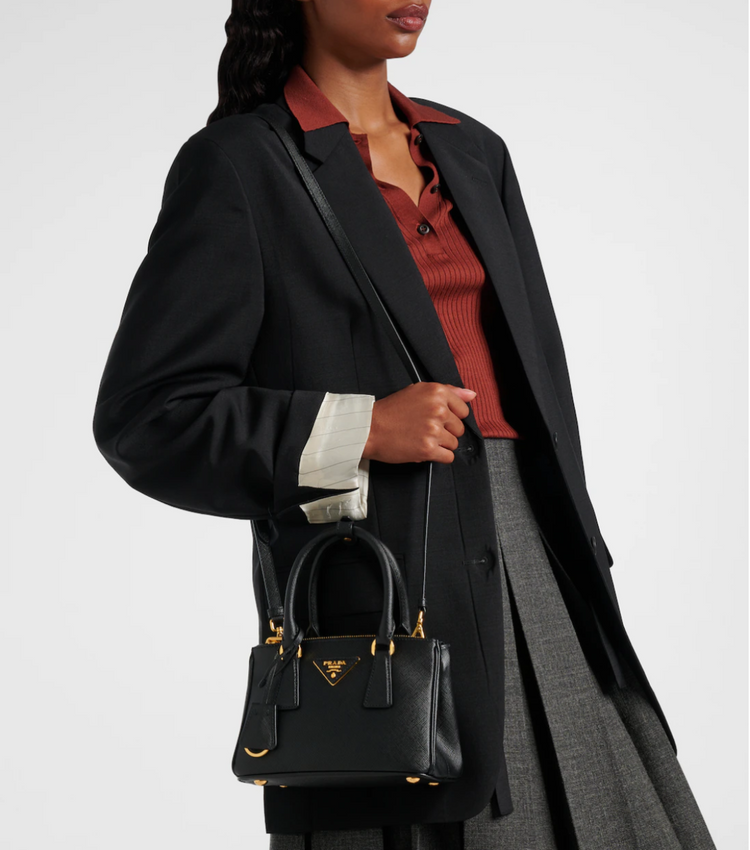 Person wearing a black coat and holding a black Pradanhandbag with a white background