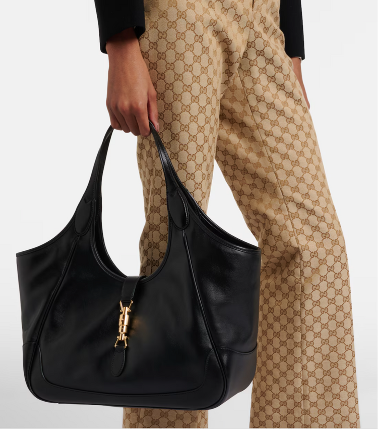 Person holding a black gucci handbag with a visible brand logo, wearing patterned pants.