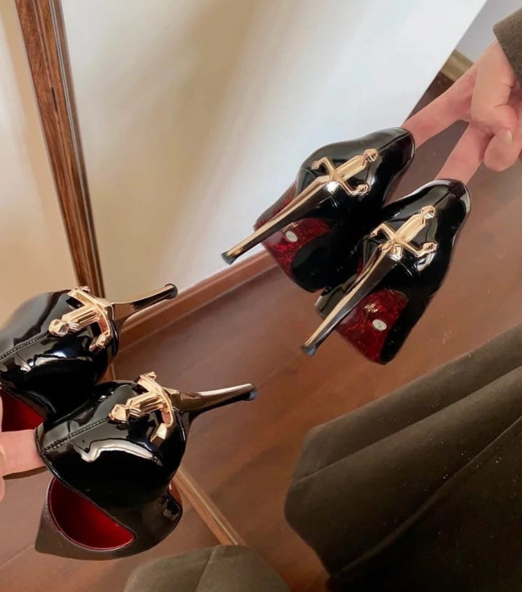 Black high-heeled shoes with gold accents held by a hand in front of a mirror.