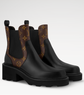 Black rain boots with brown patterned side panels on a light gray background