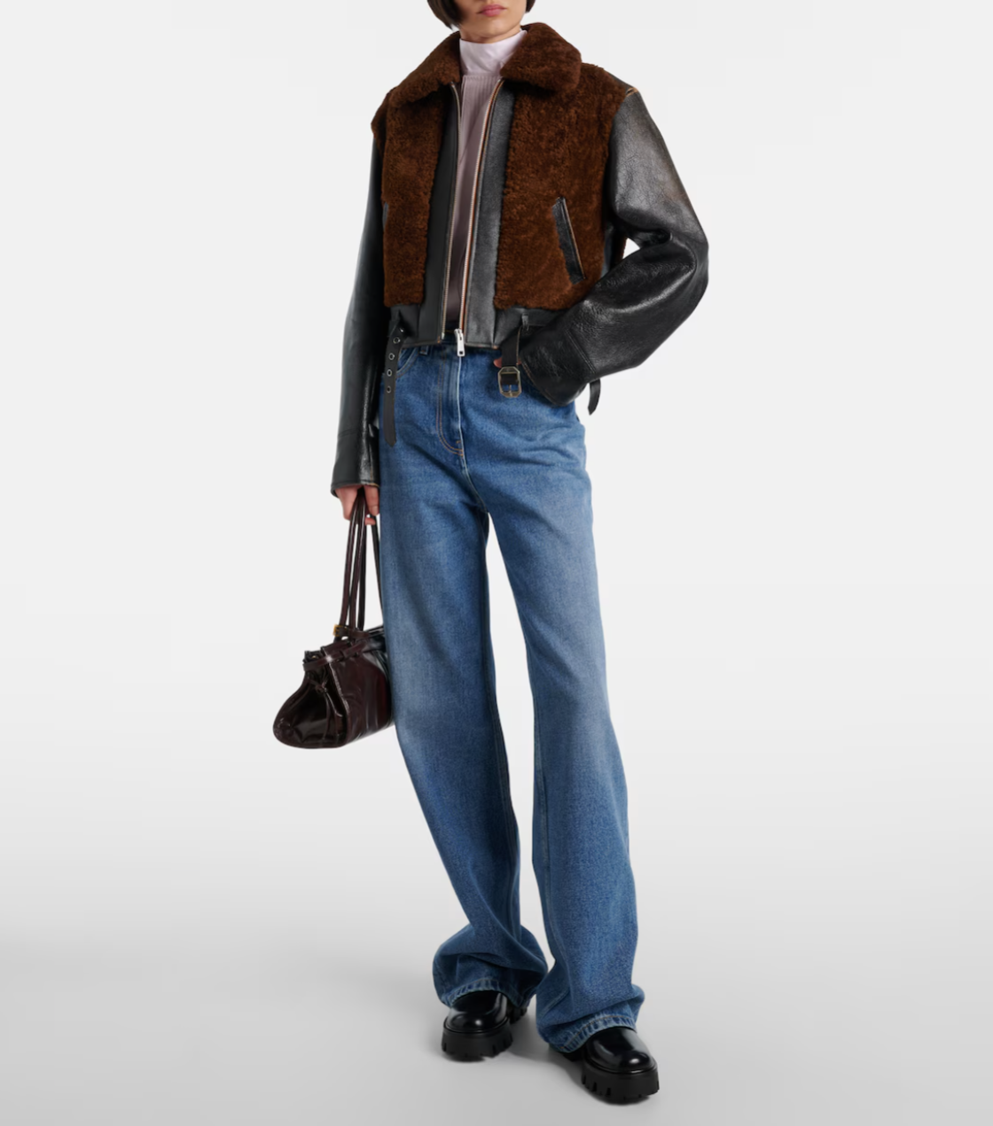 Person wearing a brown shearling jacket, blue jeans, and black shoes on a white background
