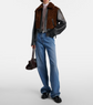 Person wearing a brown shearling jacket, blue jeans, and black shoes on a white background