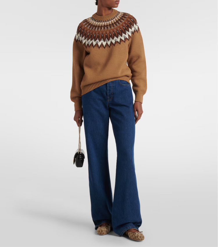 Person wearing a brown sweater with a patterned neckline and blue jeans on a white background