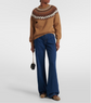 Person wearing a brown sweater with a patterned neckline and blue jeans on a white background