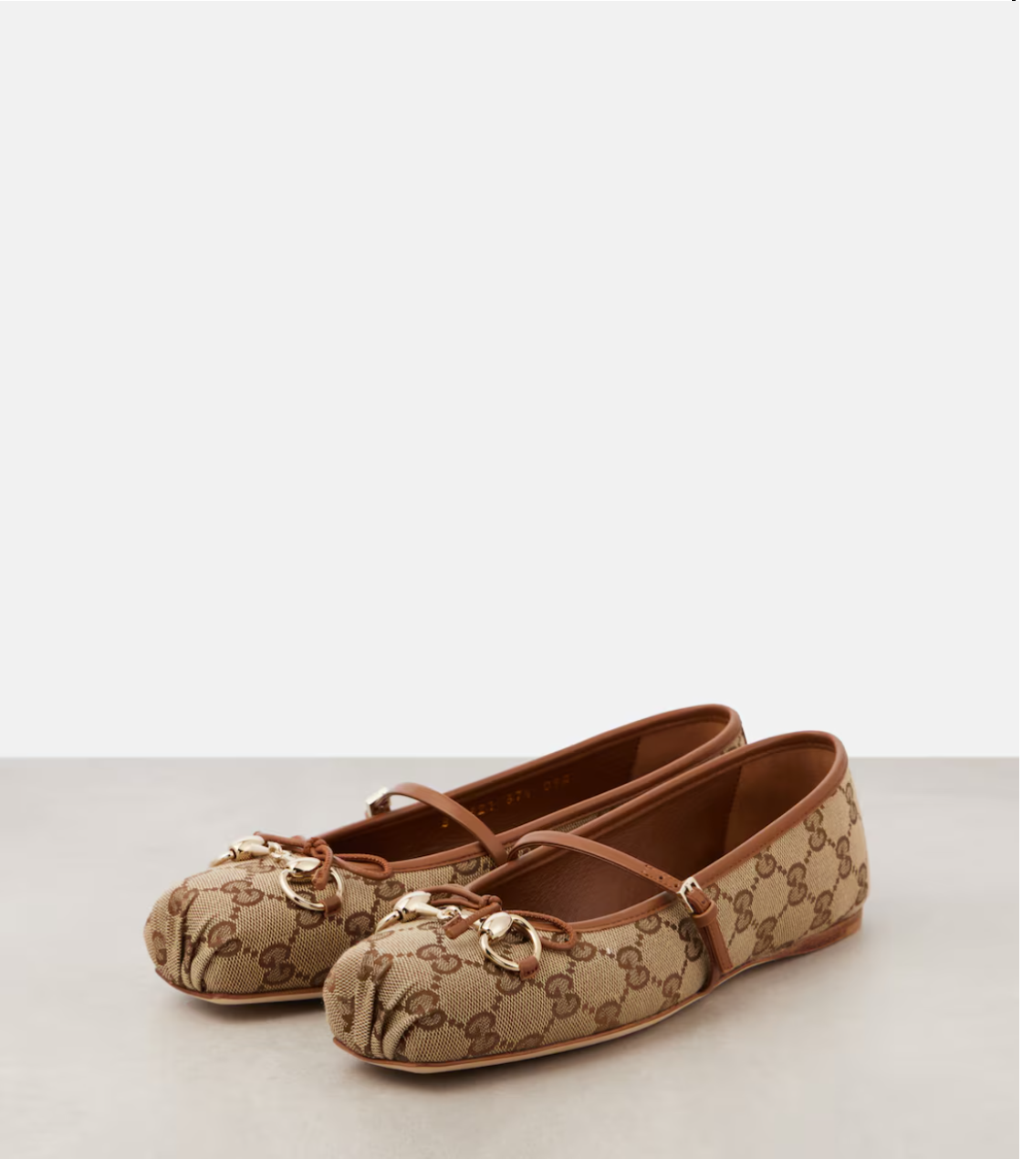 Pair of beige patterned shoes with brown straps on a light gray background