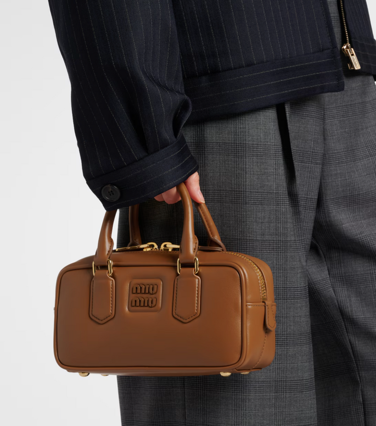 Person holding a brown leather handbag with a plain background