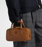 Person holding a brown leather handbag with a plain background