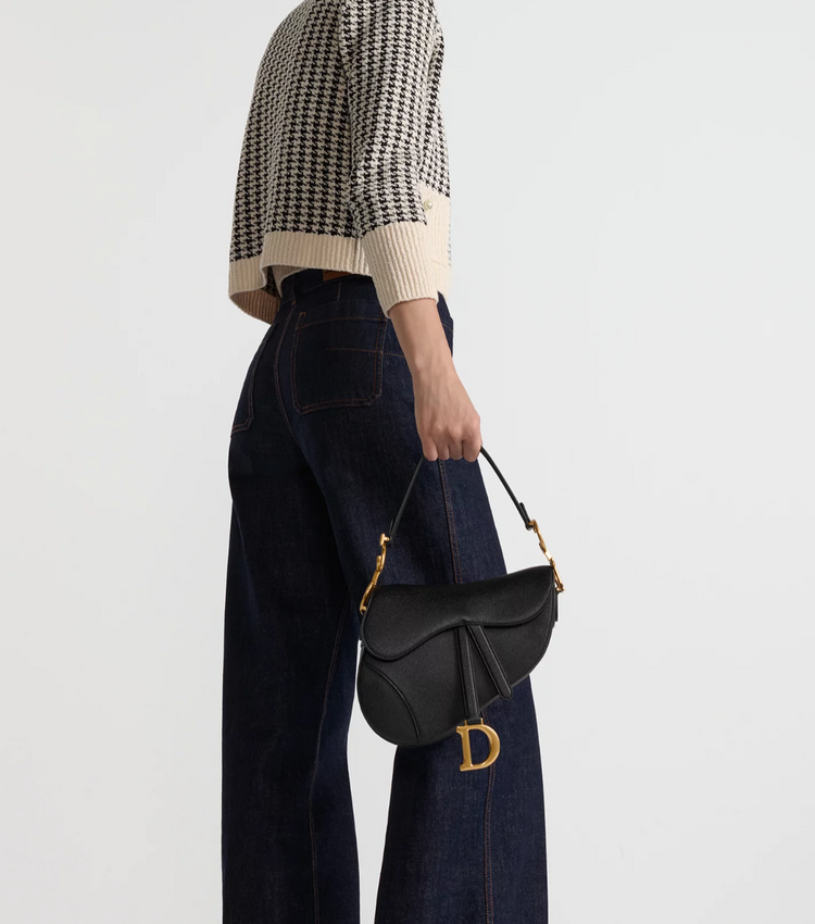 Person holding a black handbag with a gold clasp on a light gray background