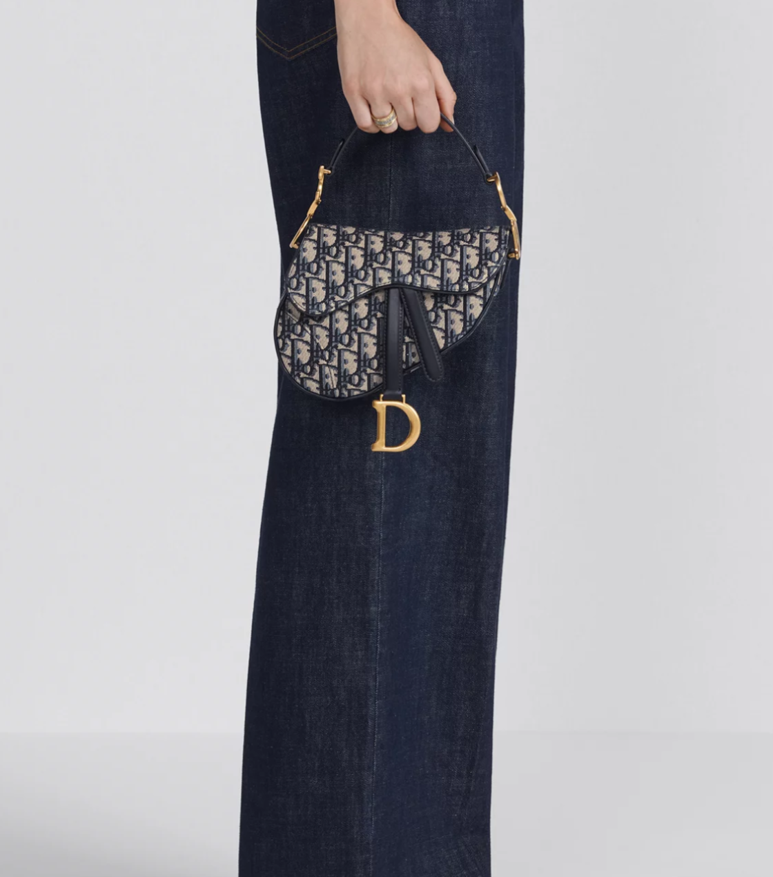 Handbag with a brand logo held by a person wearing jeans on a white background