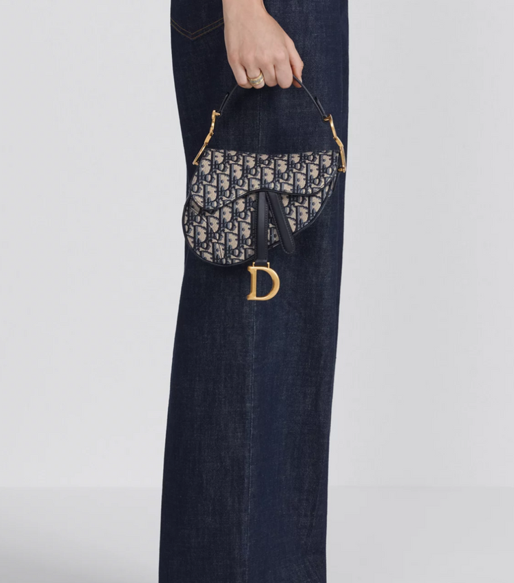 Handbag with a brand logo held by a person wearing jeans on a white background