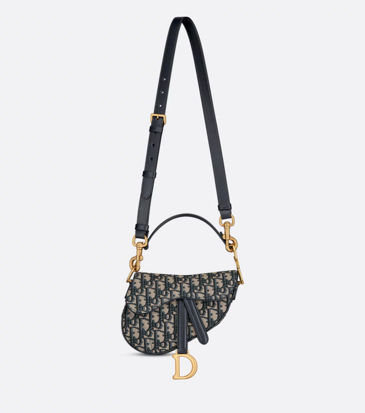 Designer handbag with black strap and gold hardware on a light gray background