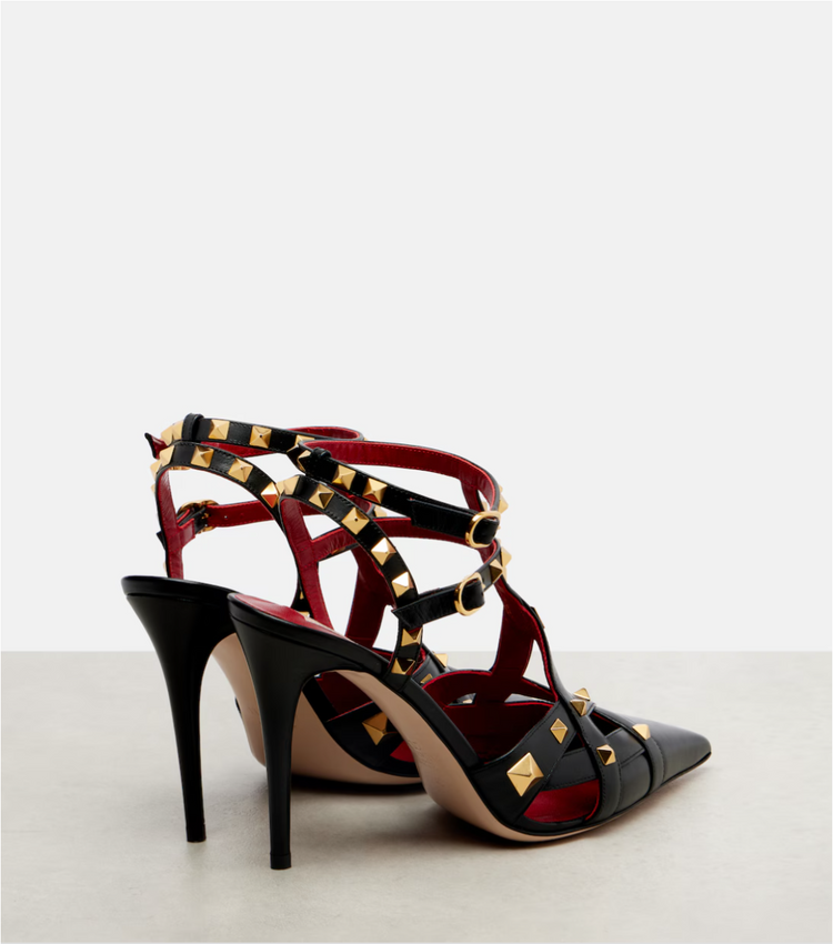 Black high-heeled shoes with gold studs on a light gray background