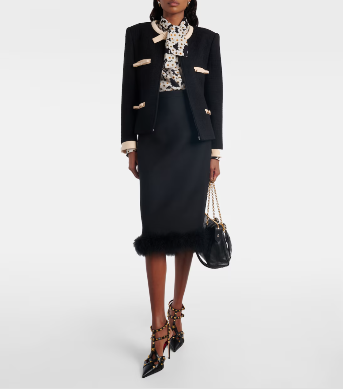 Woman wearing a black suit with a floral blouse, holding a black handbag on a white background