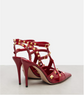 Red high-heeled shoes with gold stud accents on a light gray background