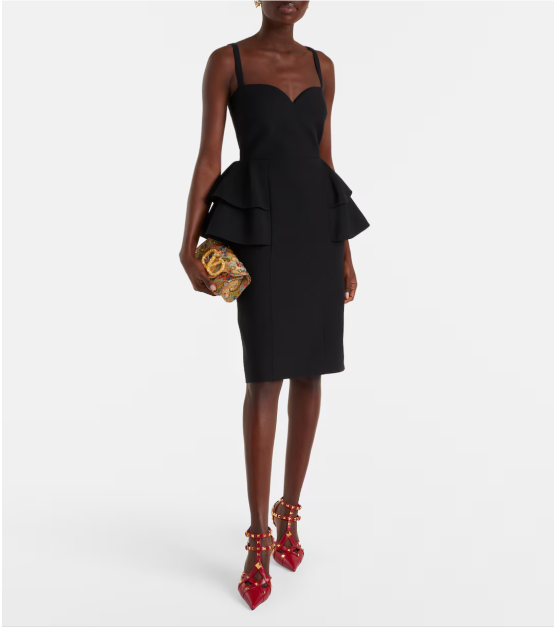 Woman wearing a black peplum dress with red high heels and a gold clutch on a white background
