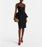 Woman wearing a black peplum dress with red high heels and a gold clutch on a white background