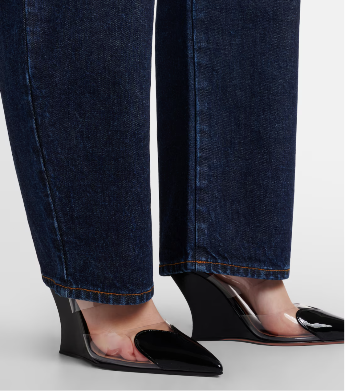 Close-up of dark blue jeans and black high-heeled shoes with clear soles on a light gray background