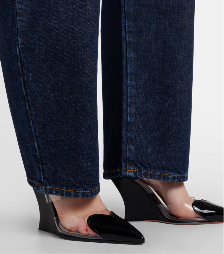 Close-up of dark blue jeans and black high-heeled shoes with clear soles on a light gray background