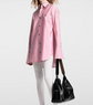 Person wearing a pink striped shirt and holding a black handbag on a white background