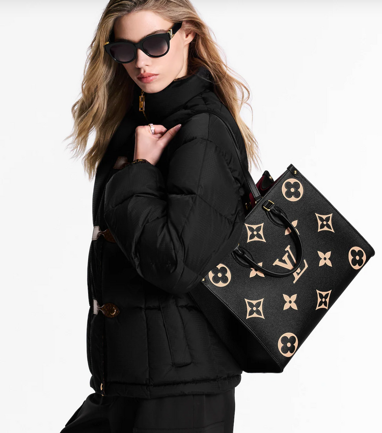 Woman holding a black handbag with gold monogram pattern against a white background