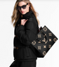 Woman holding a black handbag with gold monogram pattern against a white background