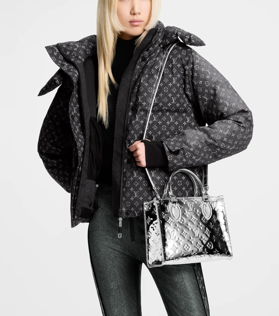 Person wearing a patterned jacket holding a transparent handbag with Louis Vuitton logo.