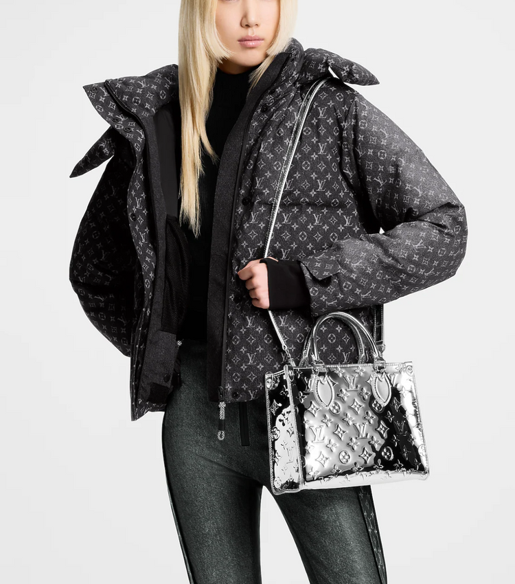 Person wearing a patterned jacket holding a transparent handbag with Louis Vuitton logo.