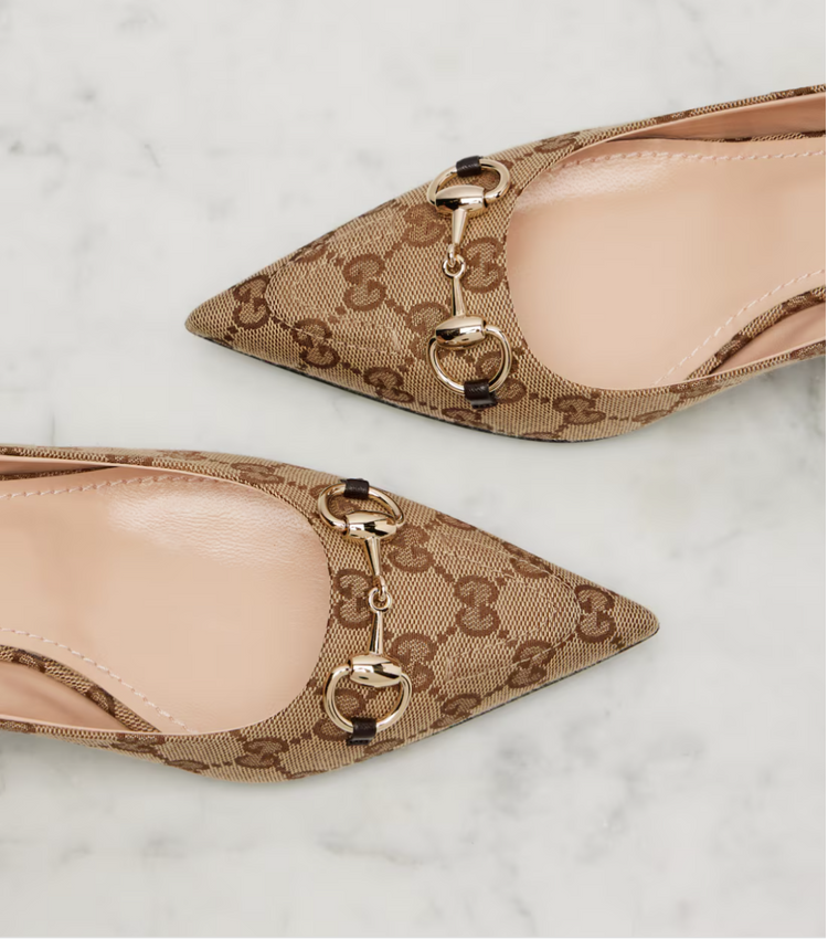 Pair of pointed-toe shoes with Gucci logo pattern on a light background