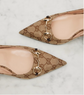 Pair of pointed-toe shoes with Gucci logo pattern on a light background