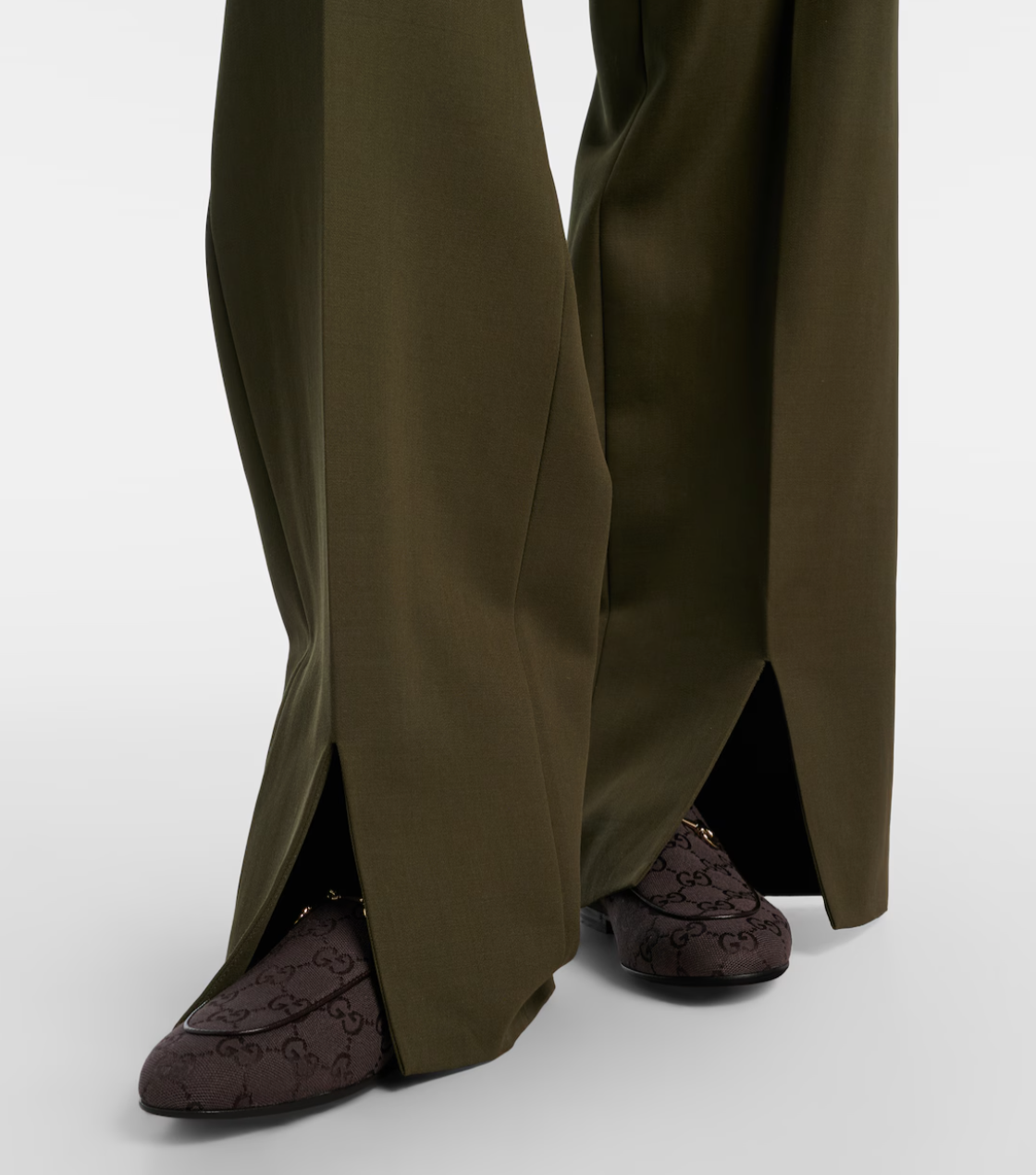 Person wearing olive green wide-leg pants and brown loafers on a white background
