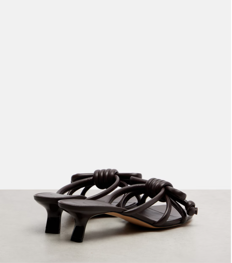 Brown high-heeled sandals with knotted design on a light gray background