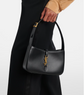 Black handbag with a gold YSL logo held by a person wearing a black coat on a white background