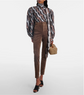 Person wearing a patterned blouse and brown pants holding a Gucci handbag and wearing black gucci mules on a white background