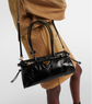 Black handbag held by a person wearing a tan coat on a light gray background