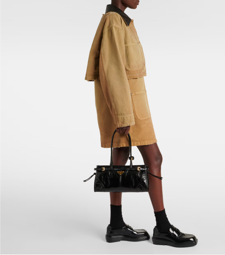 Person wearing a beige trench coat holding a black handbag on a white background