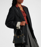 Person wearing a black coat and holding a black Pradanhandbag with a white background