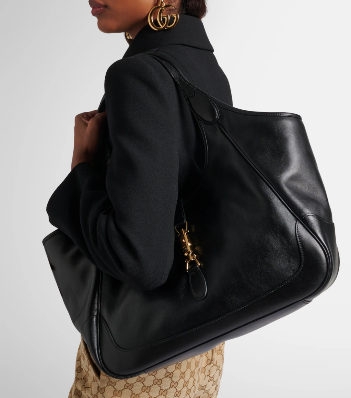 Person holding a black leather handbag with a gold clasp on a white background