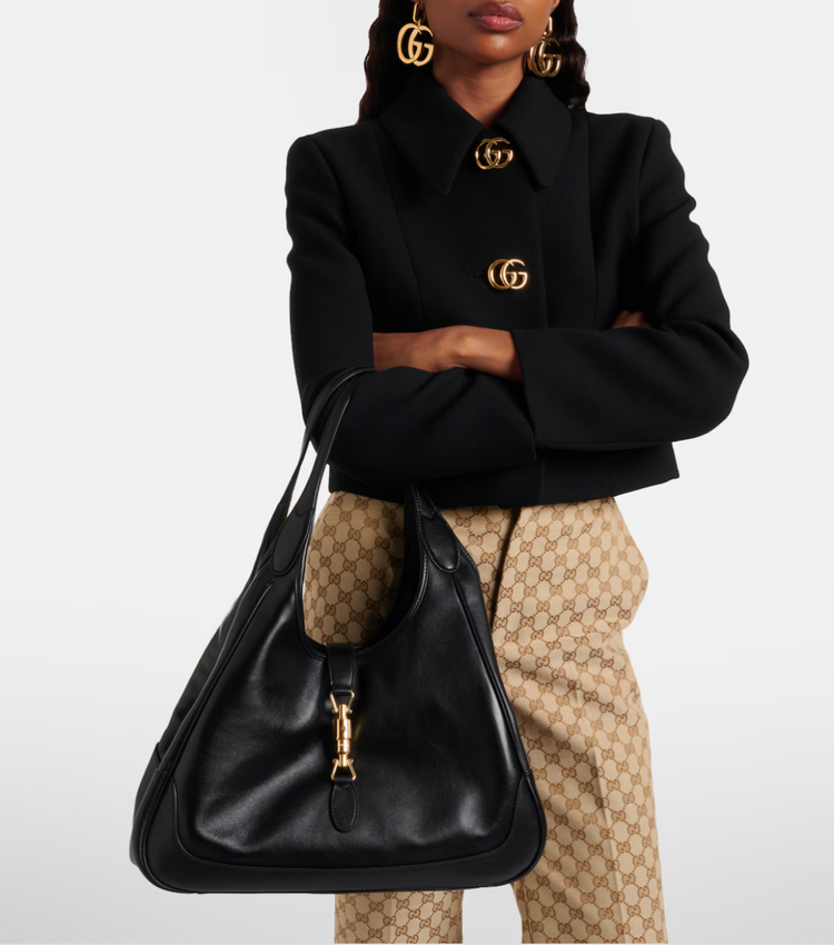 Person wearing a black Gucci coat with a black handbag featuring a small monkey plushie.