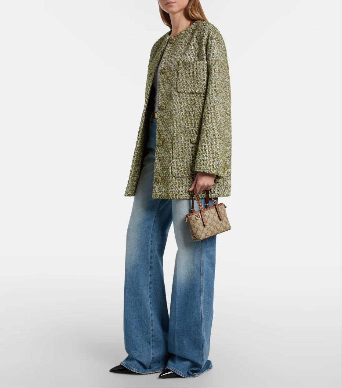 Person wearing a green patterned coat and blue jeans, holding a brown handbag on a white background