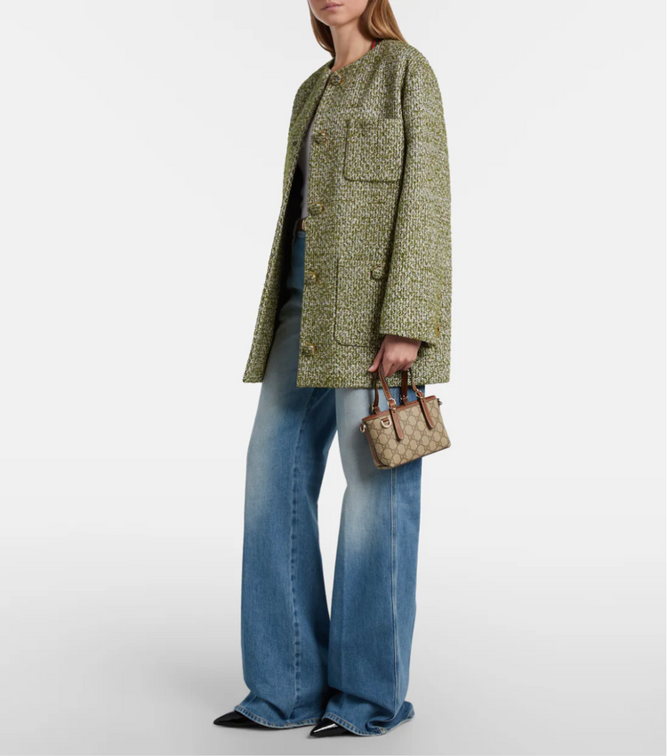 Person wearing a green patterned coat and blue jeans, holding a brown handbag on a white background