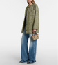 Person wearing a green patterned coat and blue jeans, holding a brown handbag on a white background