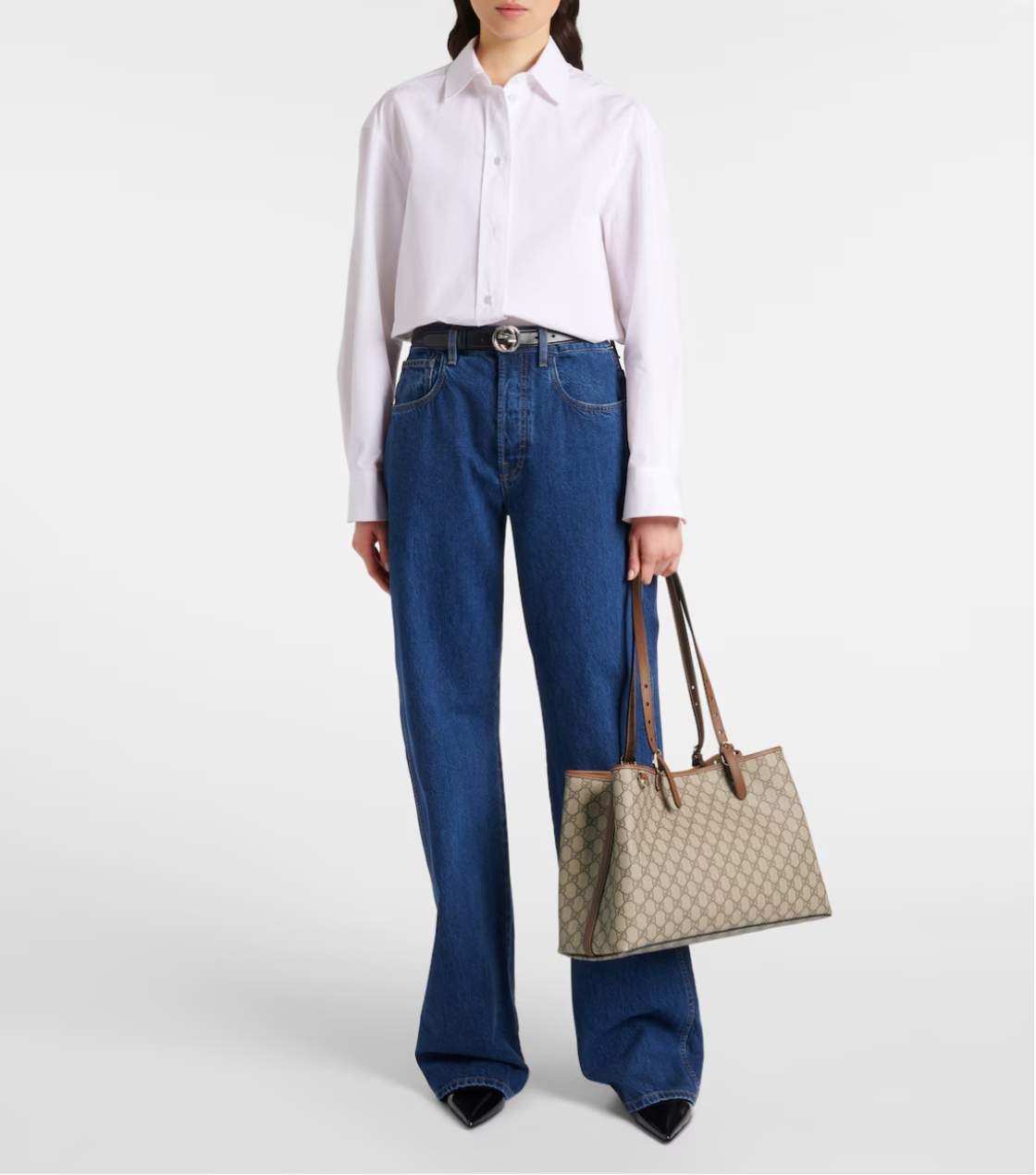 Person wearing a white shirt and blue jeans holding a beige gucci handbag on a white background