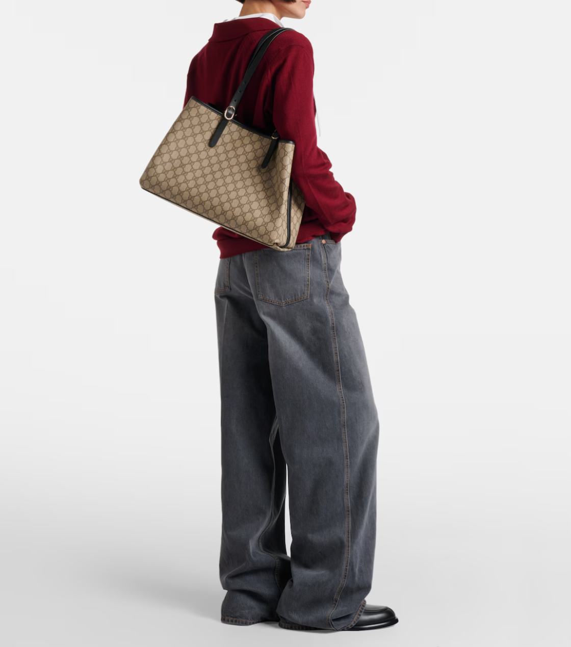 Person wearing a red sweater and blue jeans holding a beige gucci handbag on a white background