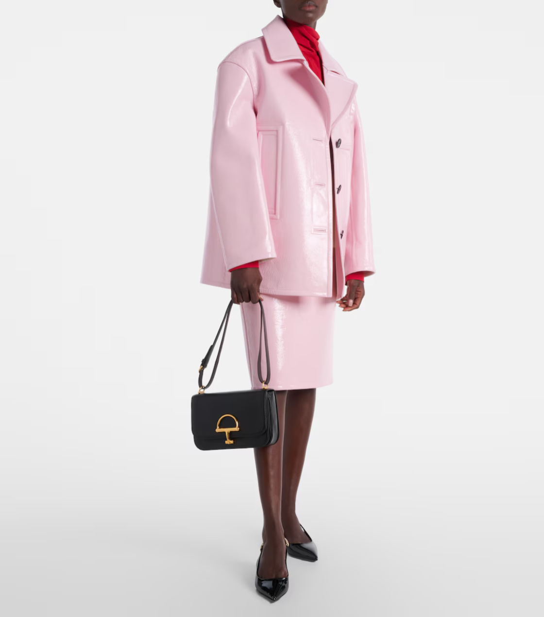 Person wearing a pink coat and skirt set with a black gucci handbag on a white background