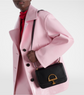 Person wearing a pink coat holding a black gucci handbag with a gold clasp on a white background
