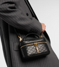Person holding a black quilted YSL handbag with gold accents, wearing a gray pinstripe suit.