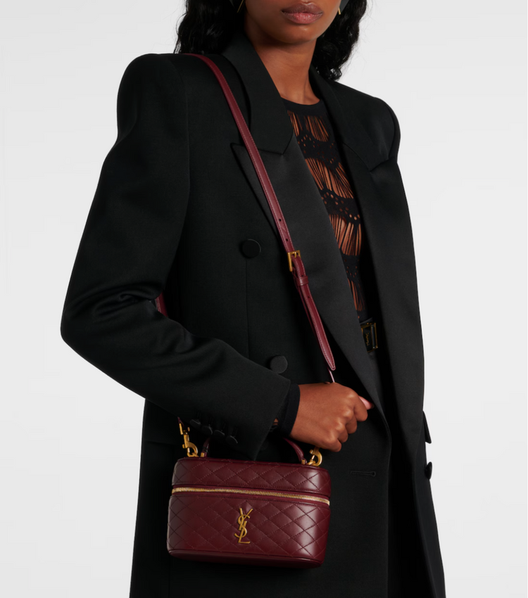 Person holding a maroon handbag with a visible ysl logo against a white background