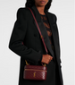 Person holding a maroon handbag with a visible ysl logo against a white background